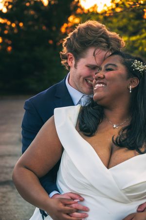 A joyful interracial couple shares a romantic wedding moment at sunset, bride in white gown, groom in navy suit.