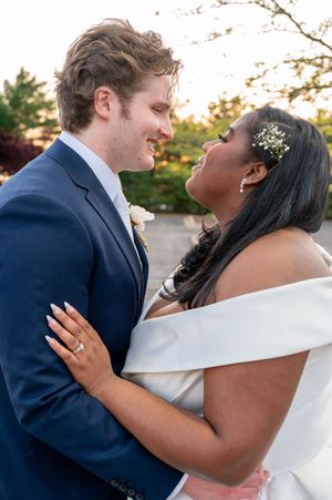 Bride and groom share a joyful moment gazing at each other, bride in off-shoulder gown, groom in navy suit.