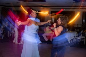 Bride in white gown dancing joyfully with a guest at a wedding reception with colorful light streaks.