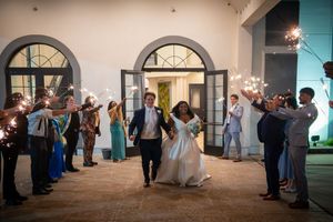 Bride and groom exit wedding reception through sparkler send-off tunnel with guests celebrating at elegant venue.