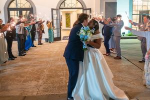 Newlywed couple sharing a kiss during sparkler send-off exit at elegant wedding venue with guests celebrating.