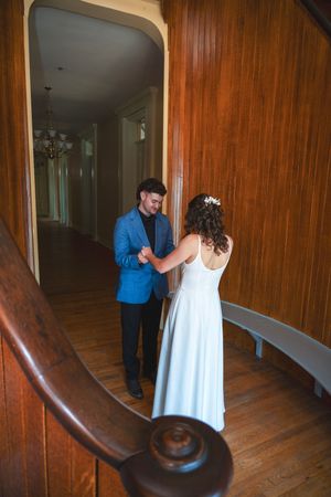 Bride and groom share a tender moment on a wooden staircase in a historic venue, with the groom in a blue suit.