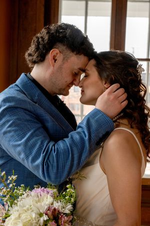 A bride and groom share an intimate forehead touch moment, with the groom in a blue plaid suit holding her face gently.