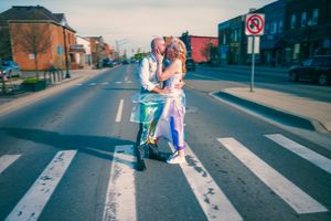 Couple kissing on a scooter at a crosswalk on an urban street, dressed in wedding attire.