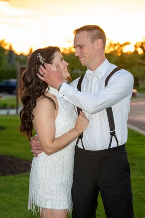 Couple in formal wear sharing a romantic moment at sunset, man in suspenders touching womans face gently.