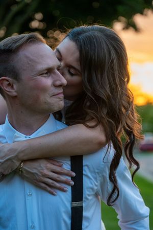 A woman kisses a man on the cheek during a romantic sunset outdoor photo session, both wearing white shirts.
