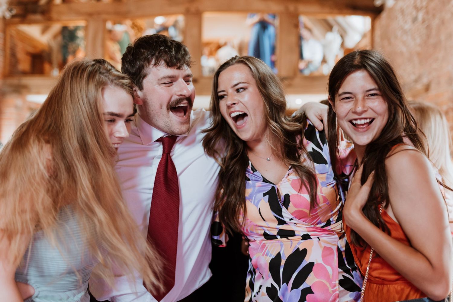 Four people laughing and smiling together at a wedding indoor celebration, dressed in formal attire on dance floor