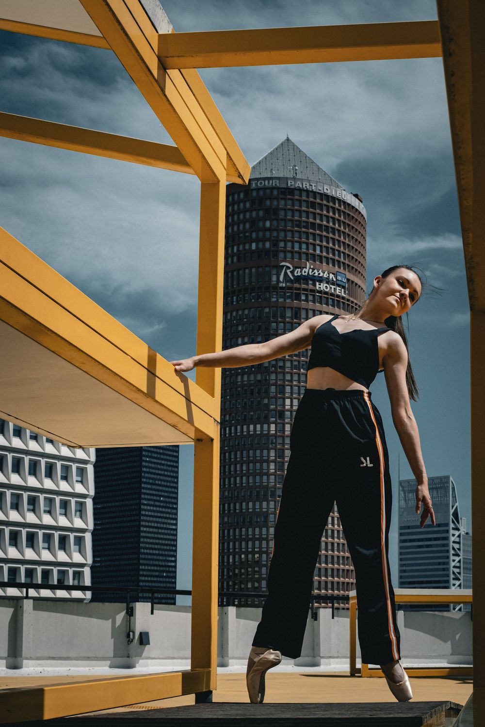 Danseuse posant sous une structure architecturale jaune devant la tour Part-Dieu à Lyon.