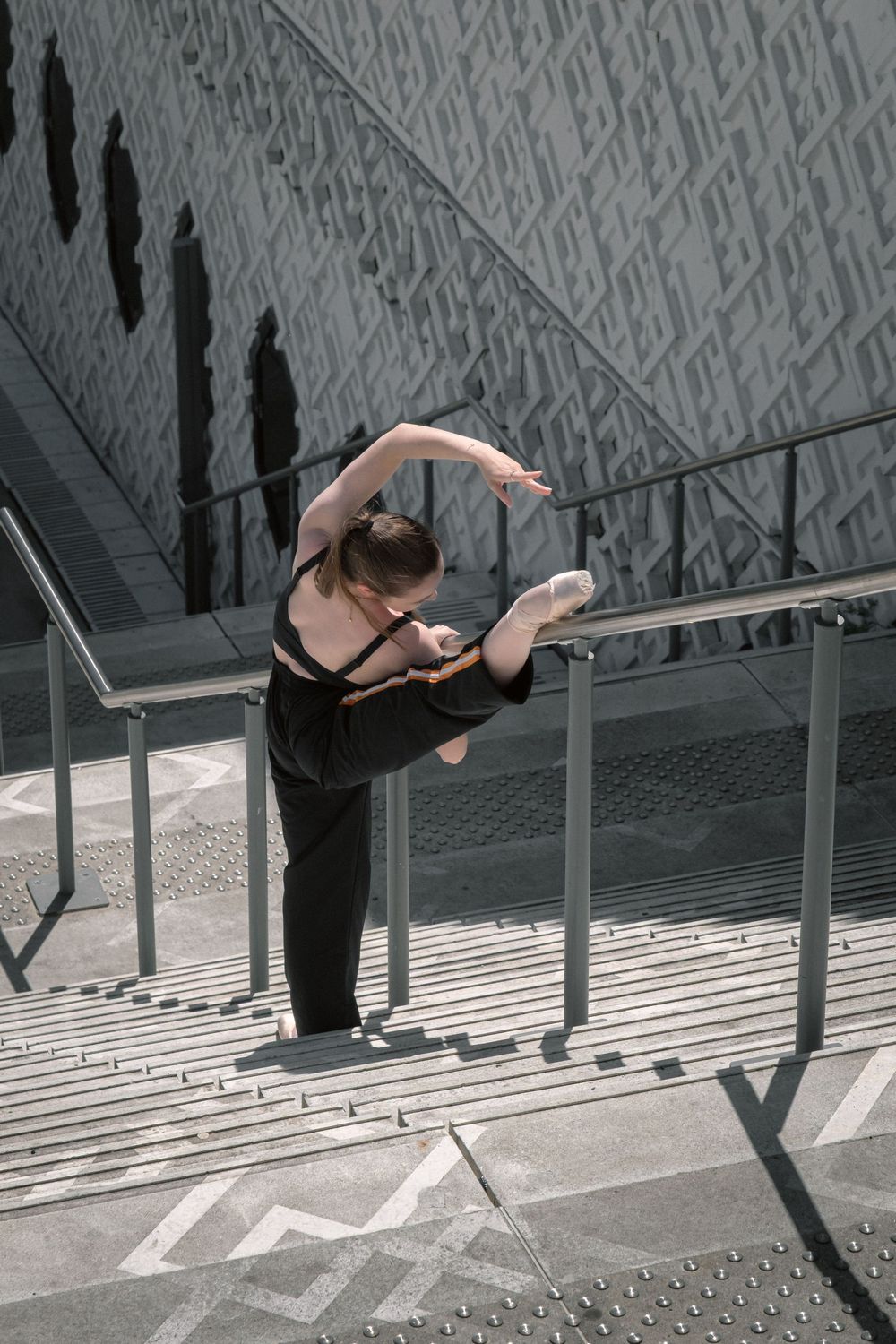 Danseuse classique penchée au-dessus d'une rambarde dans un escalier aux lignes géométriques à Lyon.