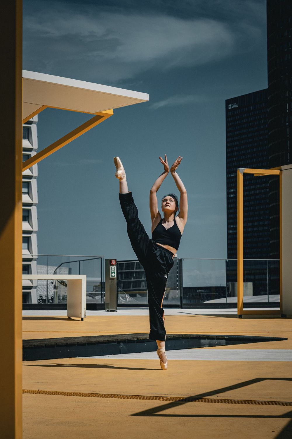 Danseuse classique réalisant une extension de jambe au milieu d'une architecture urbaine jaune à Lyon.