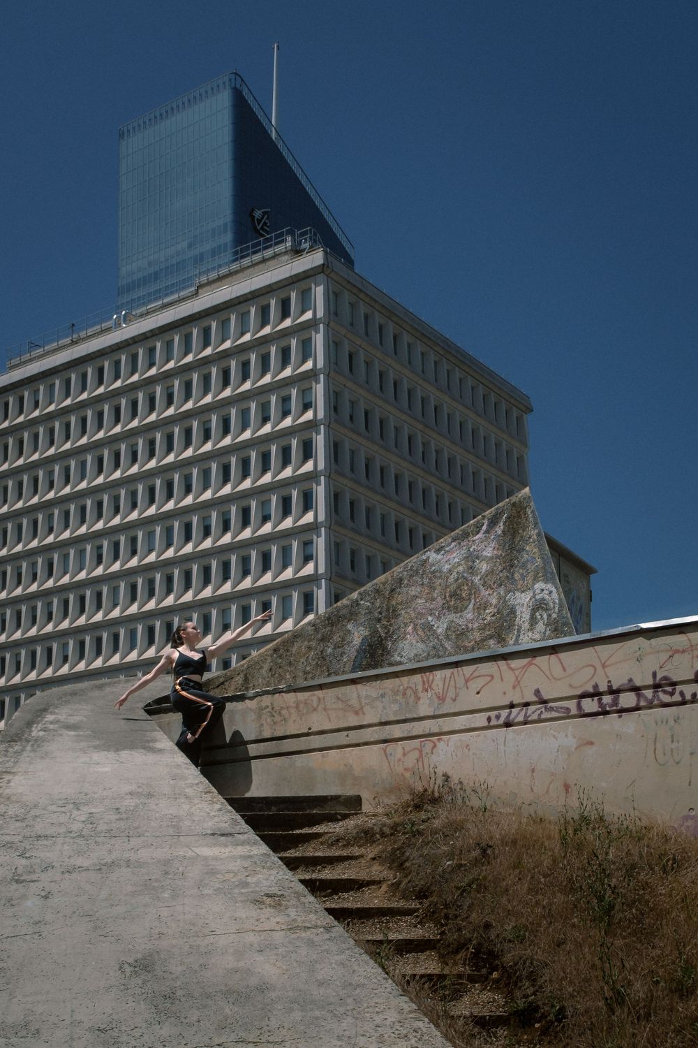 Danseuse intégrée à une architecture urbaine en béton, au pied d'un bâtiment à Lyon.