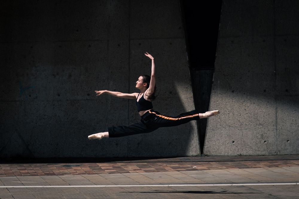 Danseuse classique réalisant un grand jeté devant une architecture en béton à Lyon.