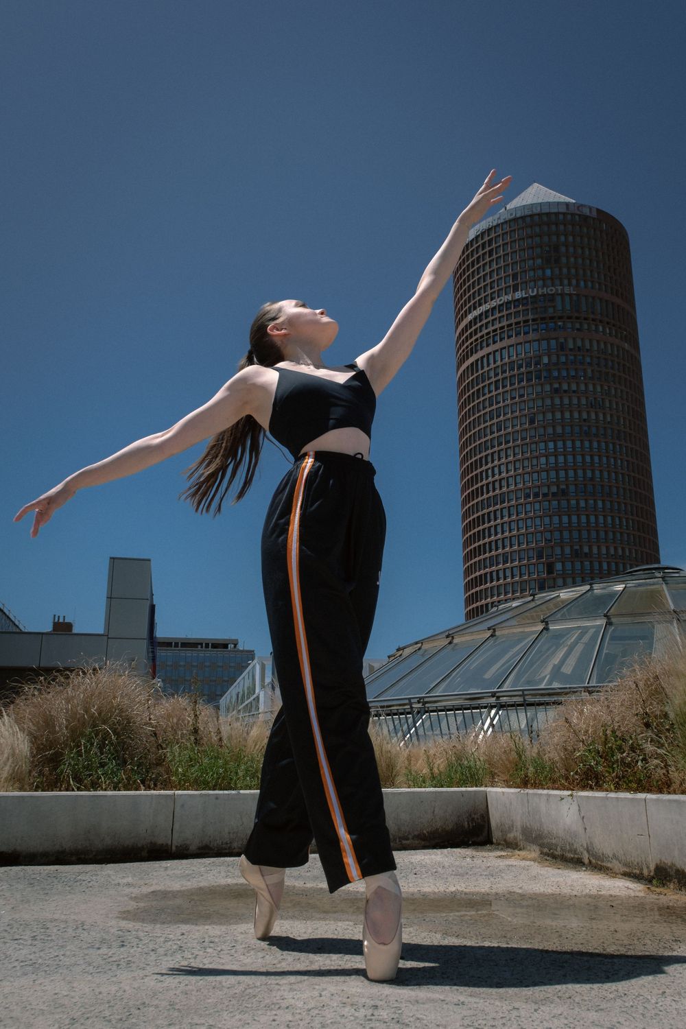 Danseuse classique sur pointes devant la tour Part-Dieu à Lyon, les bras tendus vers le ciel.