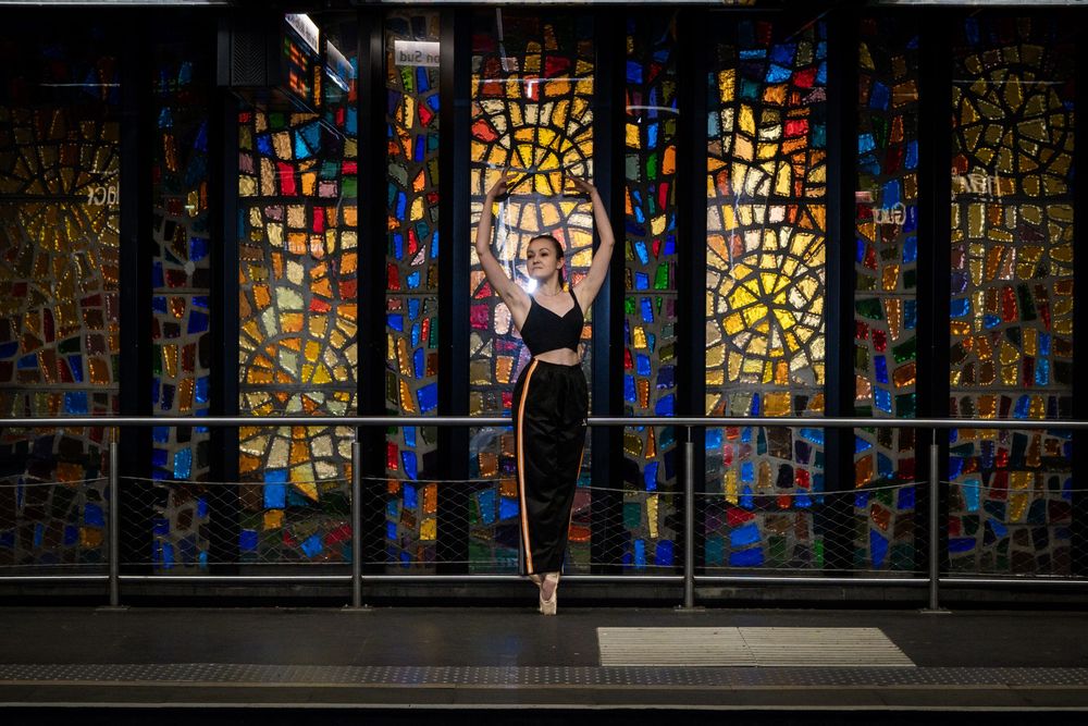 Danseuse classique sur pointes devant des vitraux colorés dans un métro à Lyon.