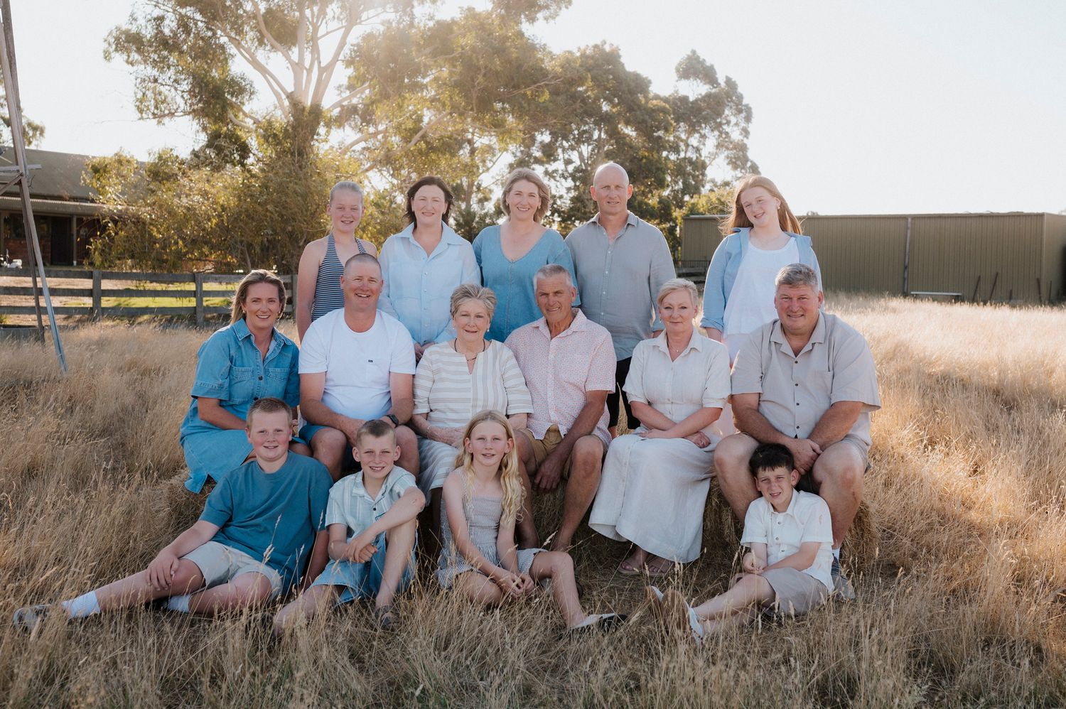 Large multigenerational family portrait outdoors in golden dry grass field during sunset in rural Australia.