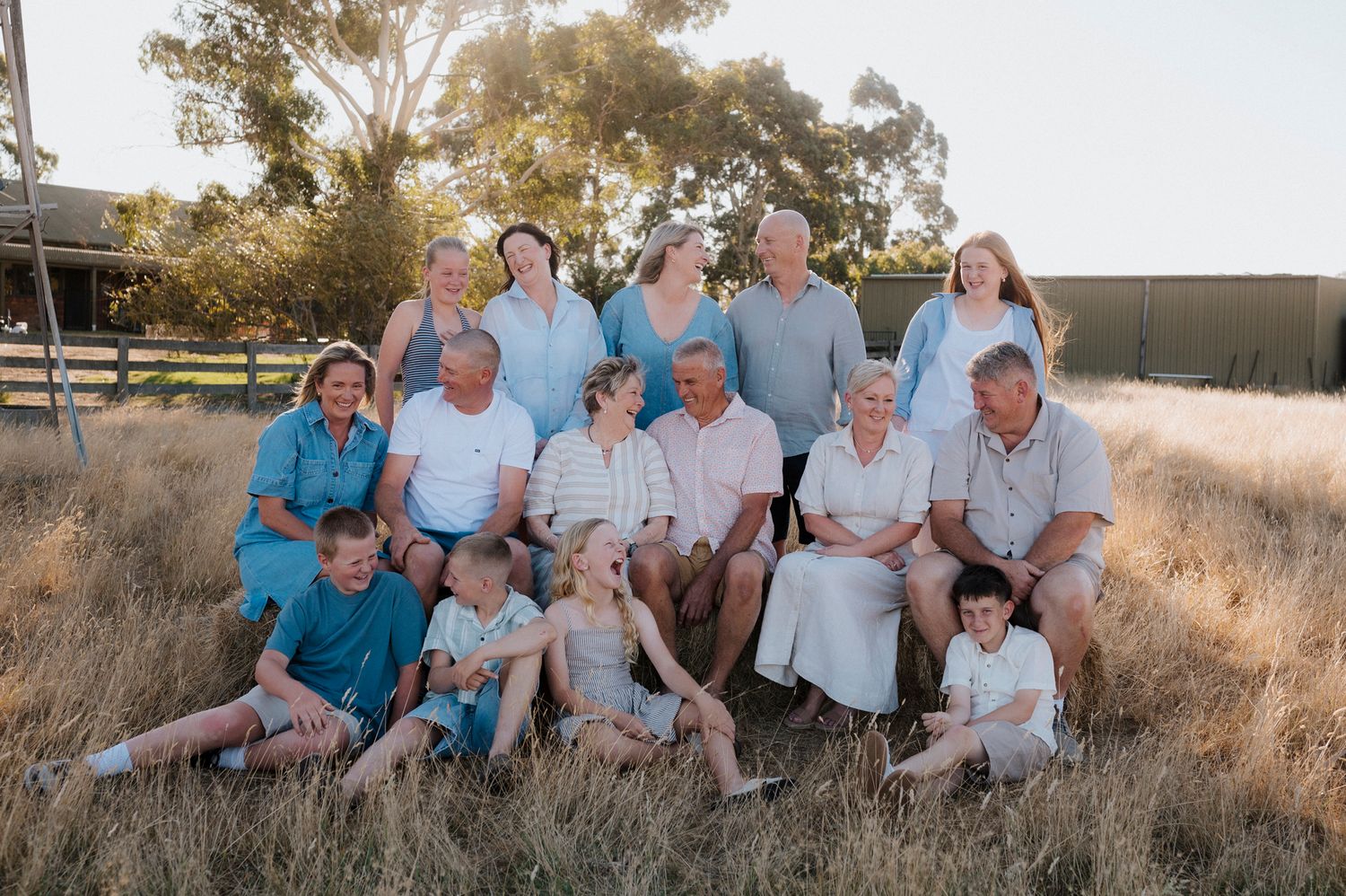 Large multigenerational family group portrait outdoors in golden dry grass field on sunny day.