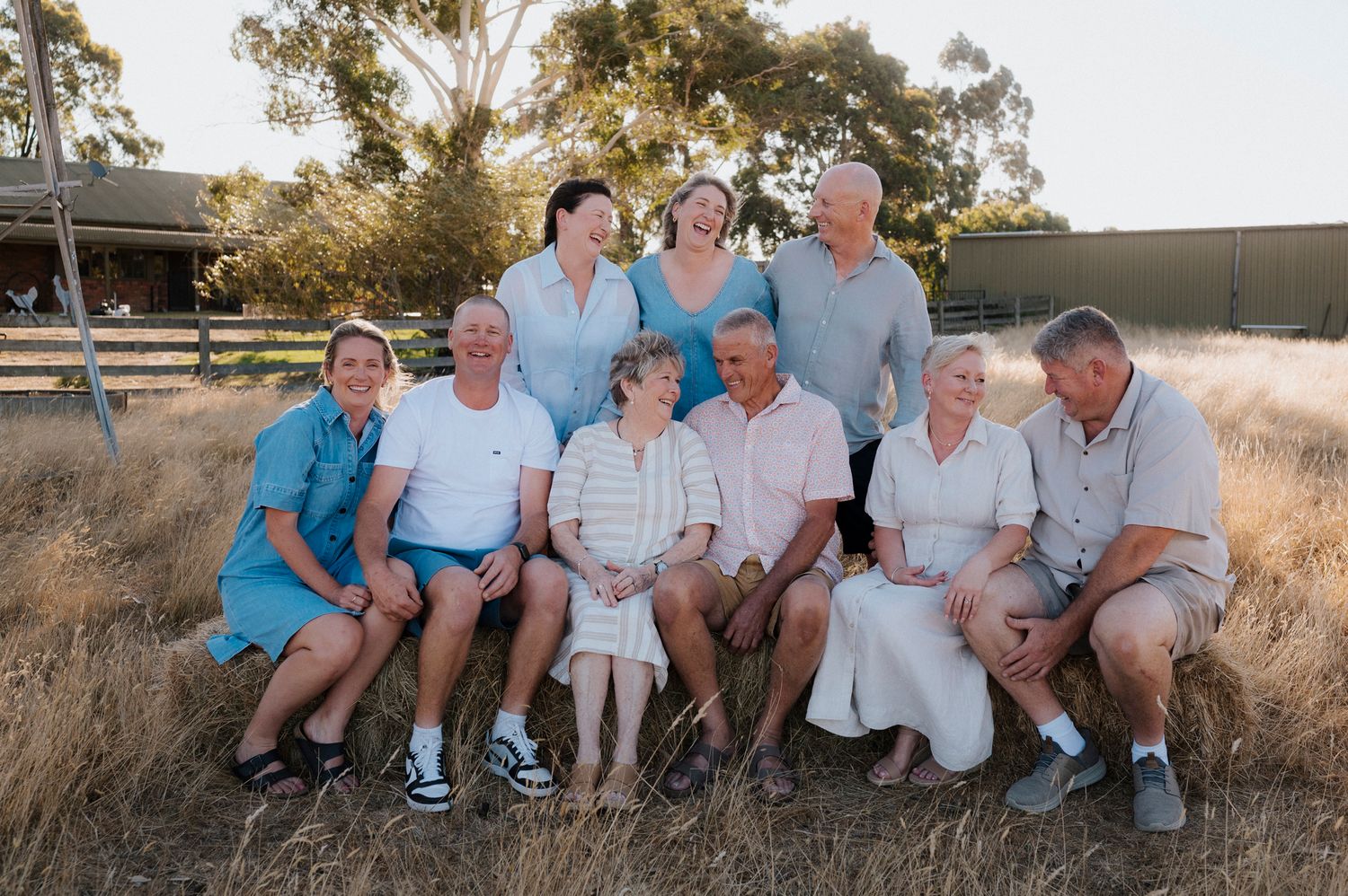Large family group portrait outdoors in golden dry grass field at sunset, multi-generational gathering smiling together.
