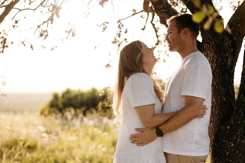 Romantic couple embracing and almost kissing under a blossoming tree in a sunny field wearing white t-shirts.