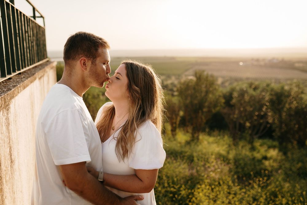 Romantic couple sharing a kiss at golden hour on a scenic overlook surrounded by lush greenery.