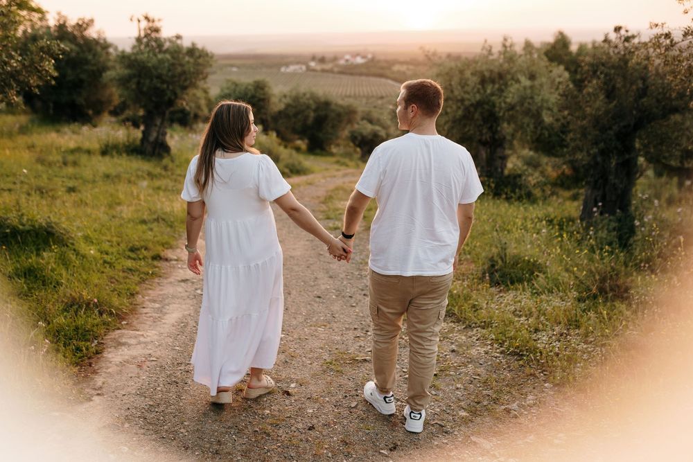 Couple holding hands walking down a rural path at sunset surrounded by lush greenery.