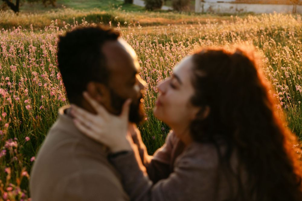 A couple shares a romantic moment about to kiss in a sunlit field of pink wildflowers at golden hour.