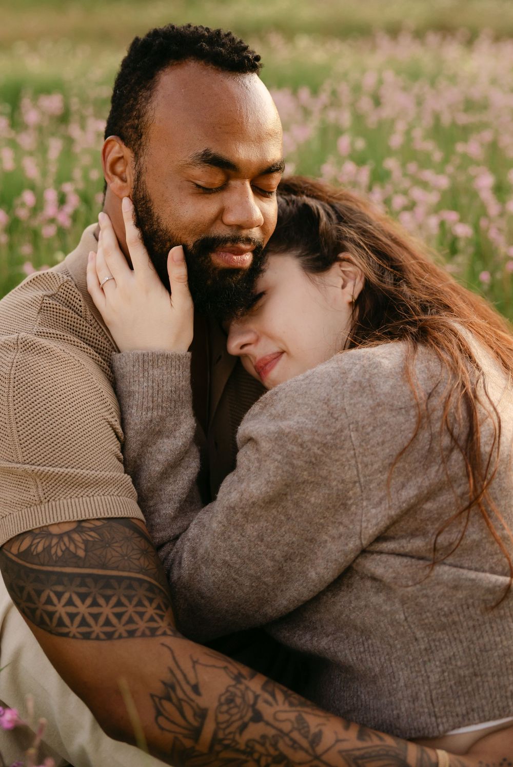 An affectionate interracial couple embraces in a blooming flower field, with the man holding the woman close.
