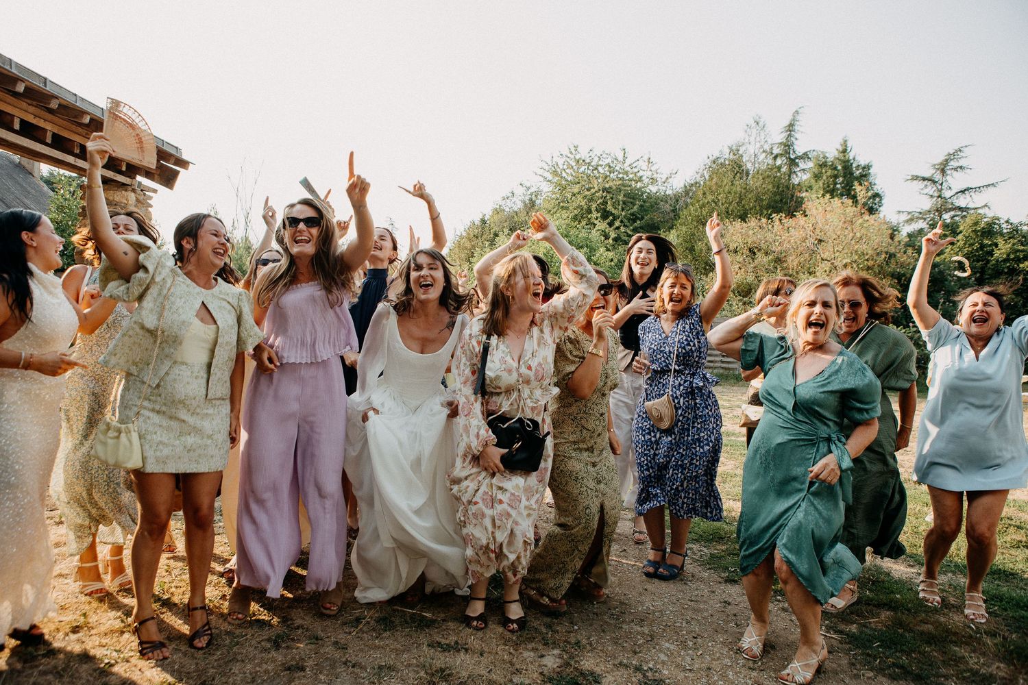 Joyful bride and female wedding guests celebrating outdoors in colorful summer dresses at a rustic garden wedding.