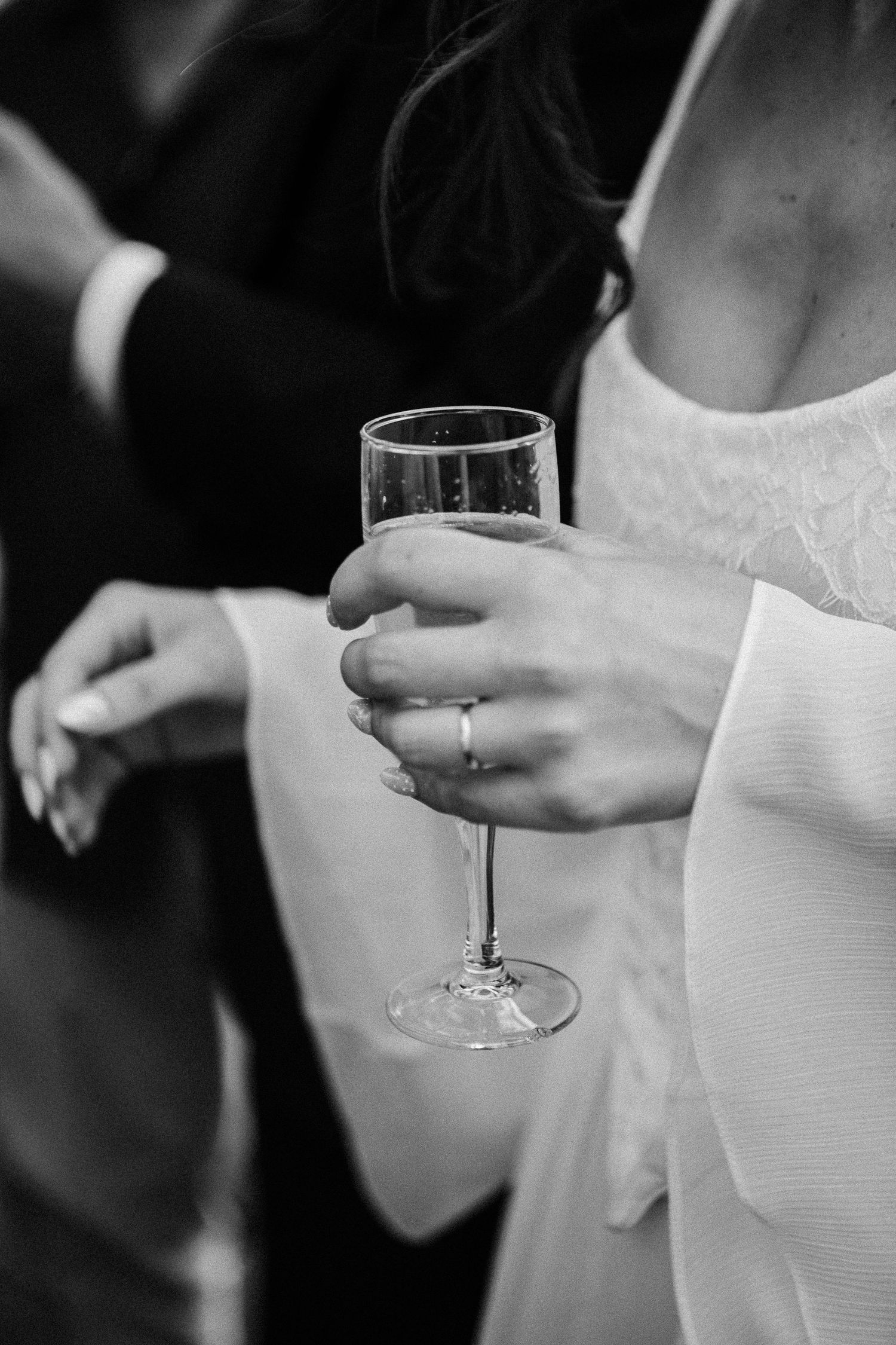 Black and white photo of a bride holding a champagne glass, wearing a wedding ring and white dress.