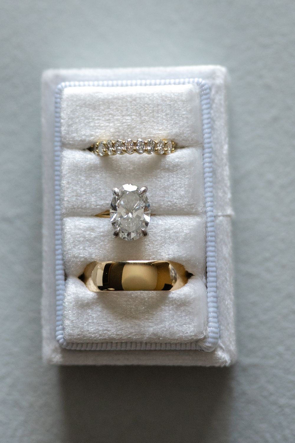 Three gold wedding rings displayed in a white velvet jewelry box, including a diamond eternity band, solitaire, and plain band.