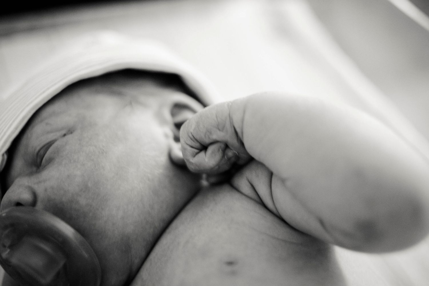 Black and white close-up of a sleeping newborn baby with tiny fist curled near face.