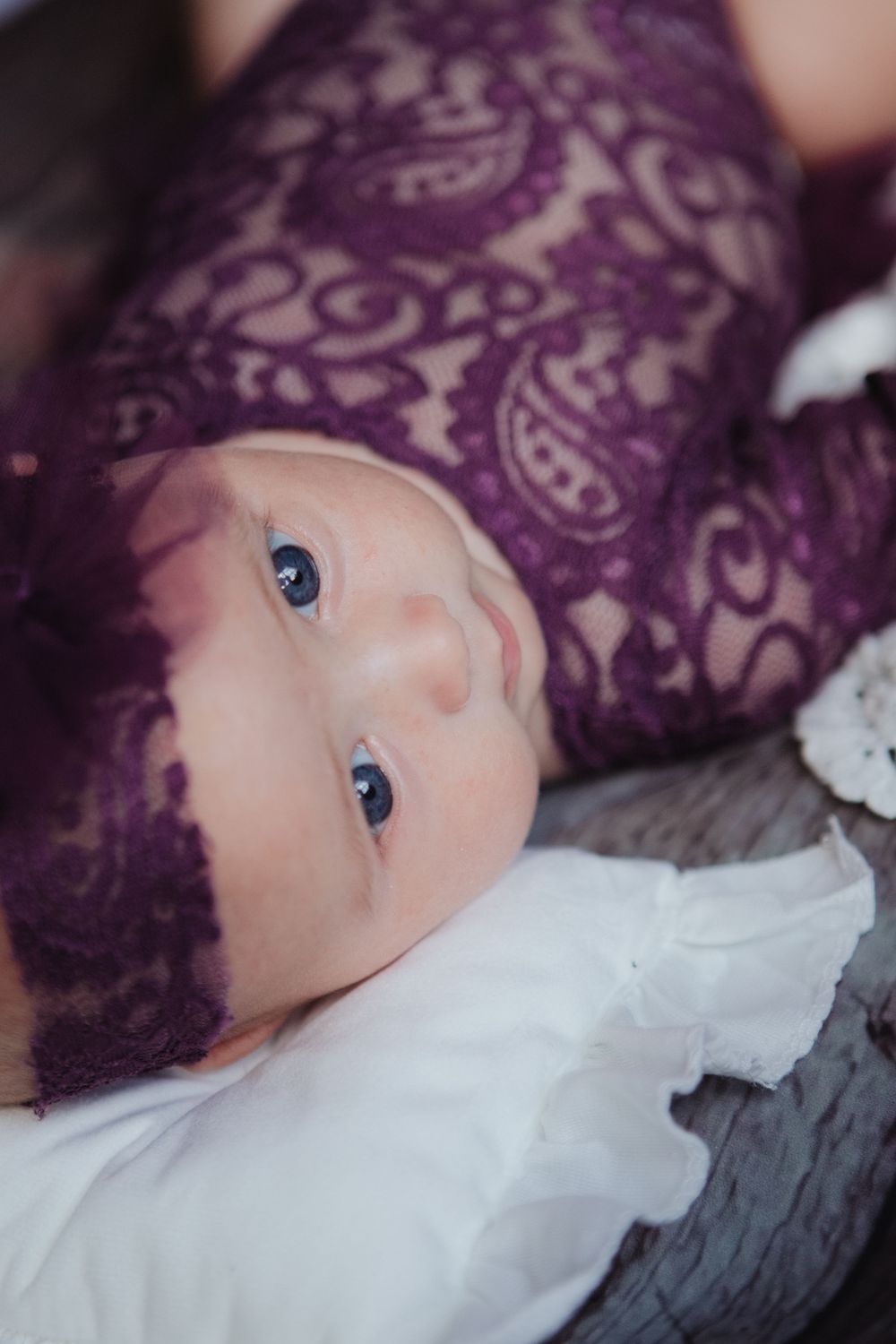 Close-up of newborn baby girl with blue eyes in purple lace wrap and headband.