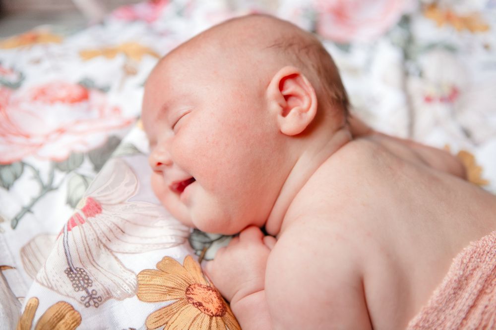 Smiling sleeping newborn baby lying on floral blanket in soft natural light.