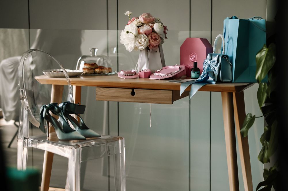 Elegant wooden desk styled with pink roses, teal heels, gift bags, and beauty accessories in a chic feminine setting.