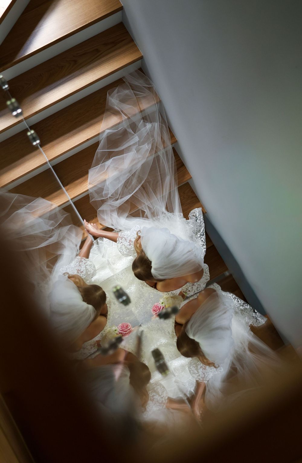 Aerial view of a bride in white gown and veil surrounded by bridesmaids in white dresses, captured from above a staircase.