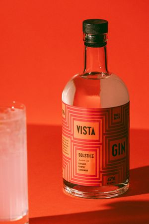 Vista Gin Solstice bottle with green cap on red background, 47% alcohol, beside a glass with ice.