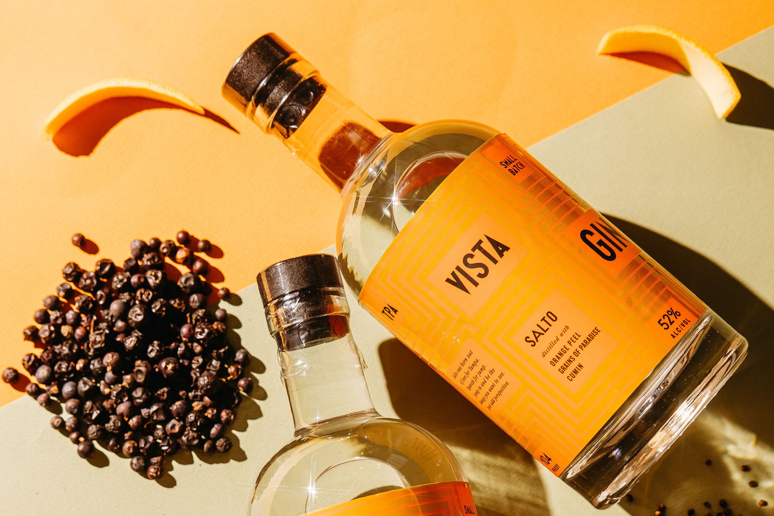 Vista Salto gin bottle with juniper berries and orange slices on a warm amber background.