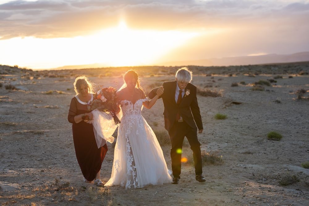 Wedding party celebrating at sunset in a desert landscape, bride in white gown with family members in formal attire.