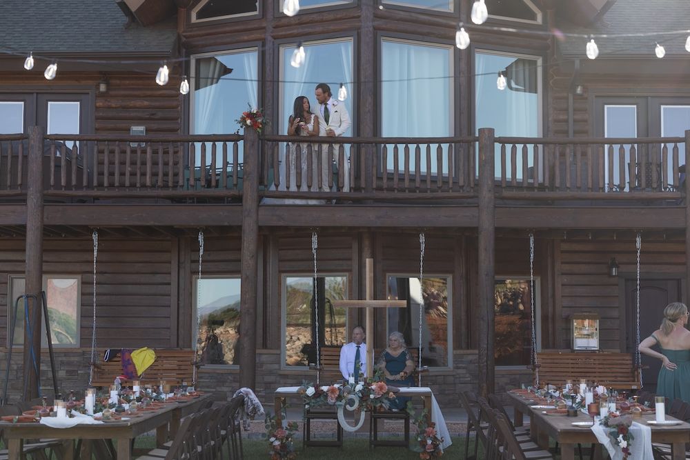 Rustic log cabin venue with outdoor dining tables and couple on balcony, perfect for weddings and events.