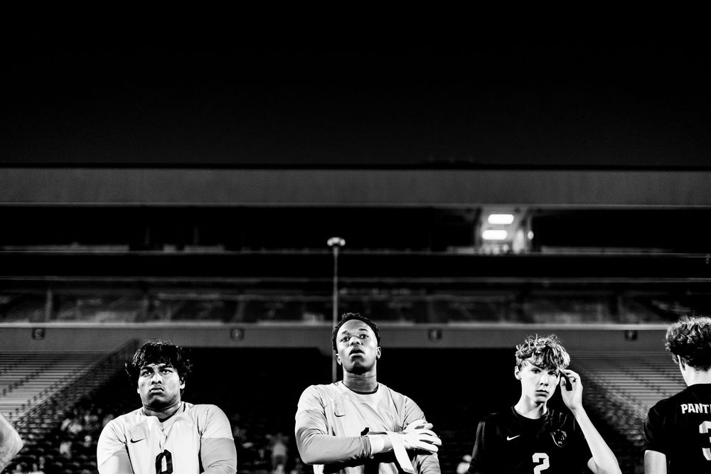 Black and white photo of three soccer players standing solemnly on field under stadium lights at night.