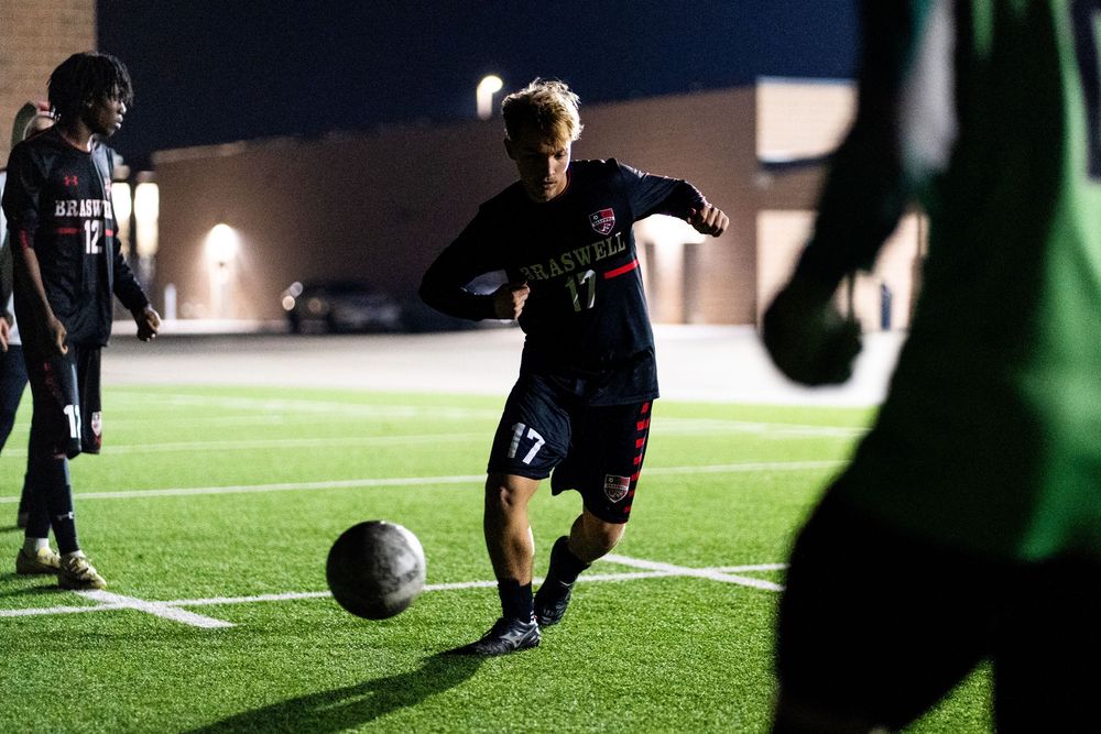 Soccer player number 17 in dark uniform practicing ball control under bright stadium lights at night.