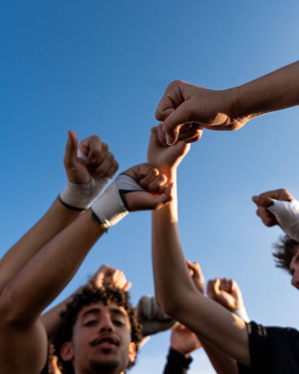 Low angle view of soccer team raising fists together in team huddle against clear blue sky.