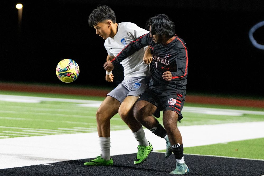 Two soccer players aggressively competing for possession of ball during intense nighttime match on field.