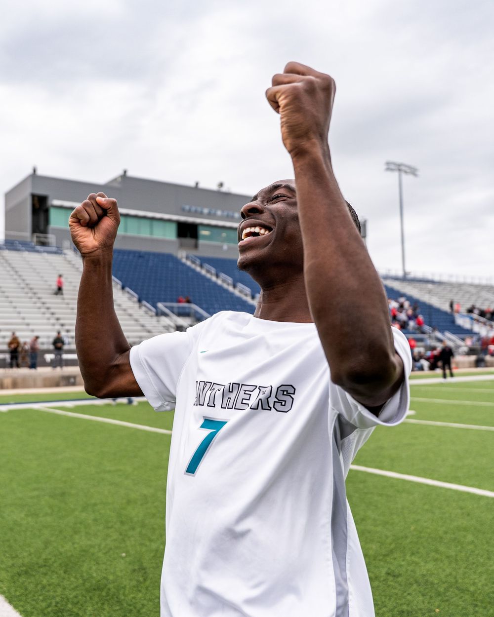 Soccer player wearing number 7 jersey celebrating victory with raised fists on stadium field.