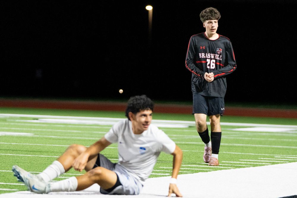 Two soccer players on field, one sitting on ground after a challenge during match.