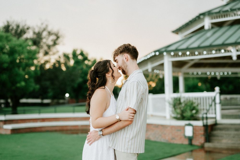Couple sharing a romantic moment at sunset near a white gazebo on a lush green lawn.