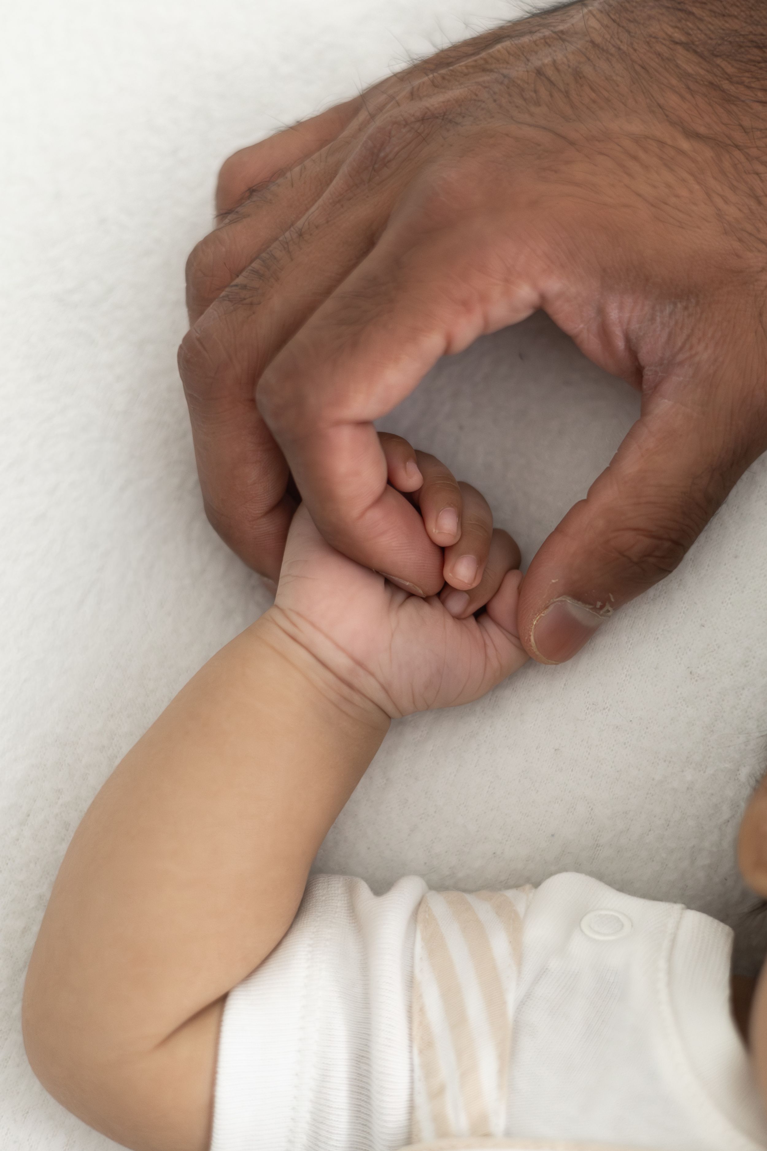 A baby's tiny hand gripping an adult's finger on a white blanket, symbolising love and connection Nottingham newborn photographer