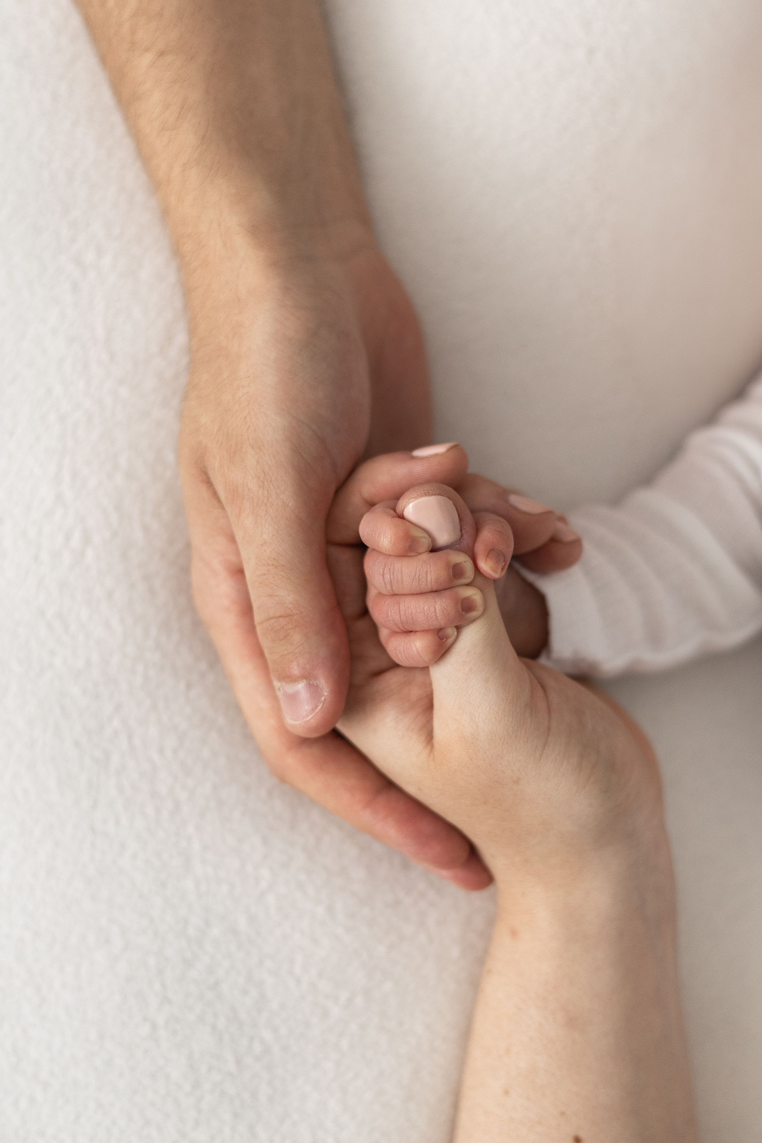 Two adult hands gently cradling a tiny newborn baby hand, symbolising love and family bond Nottingham newborn photographer