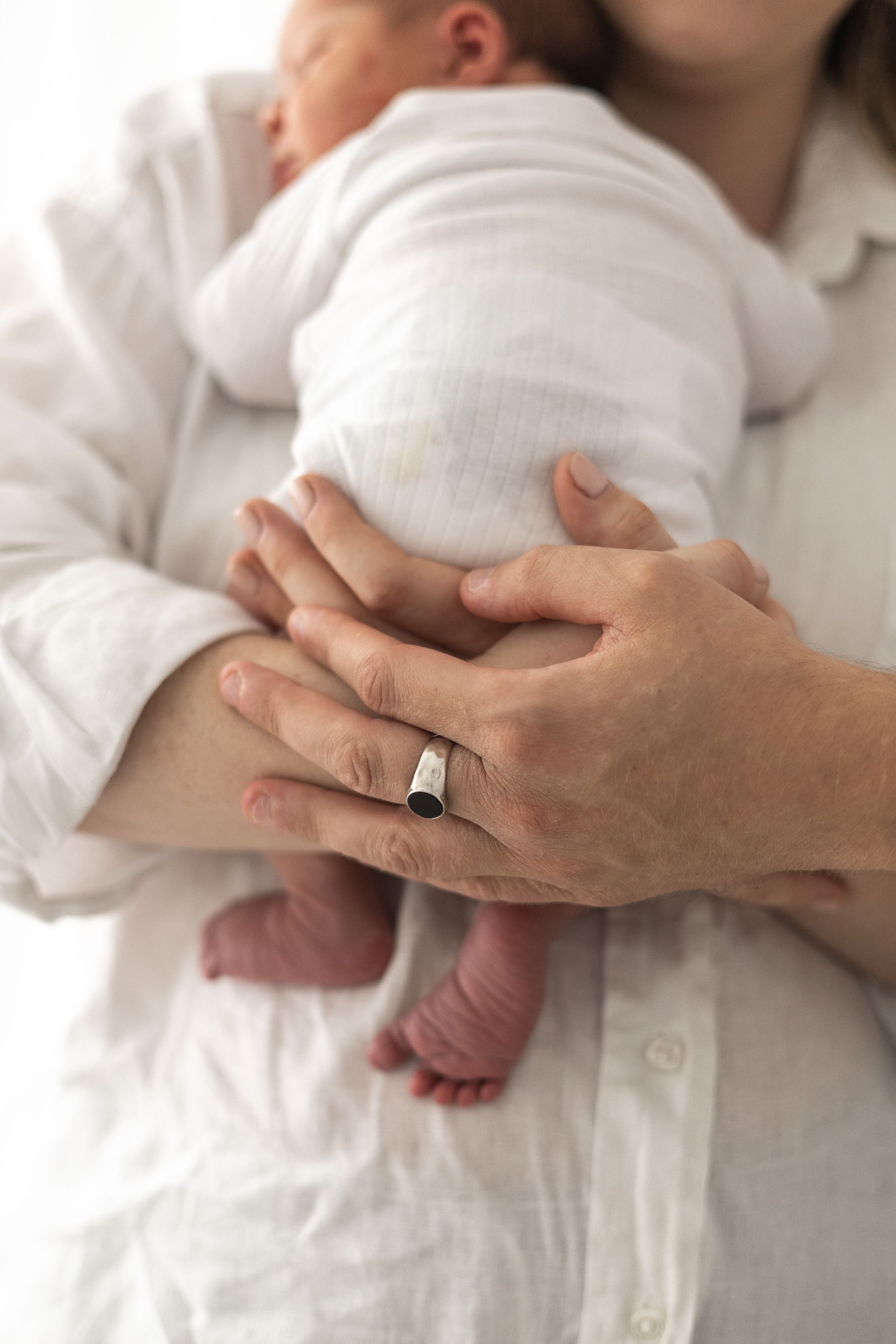 Parents cradling a newborn baby in white clothing, Nottingham newborn photographer