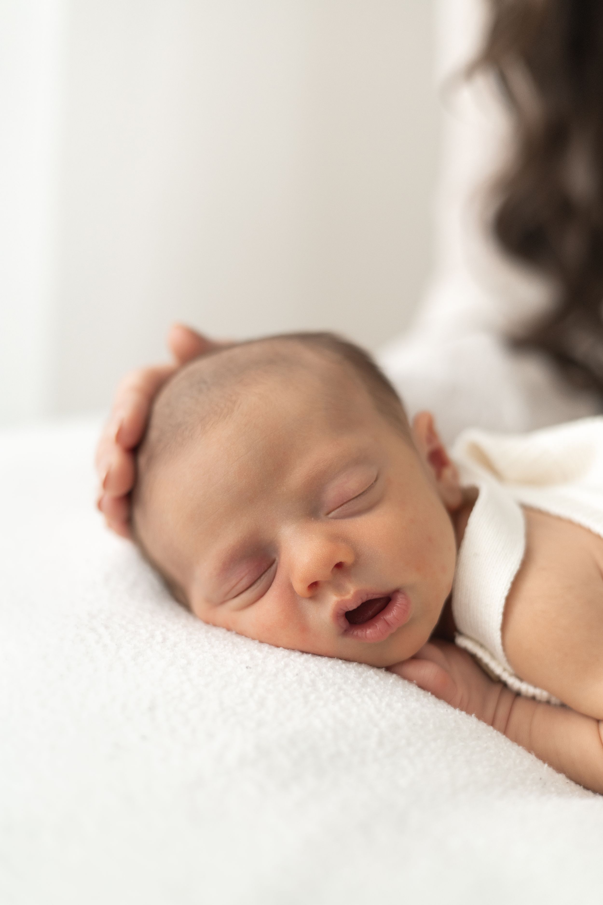 A newborn baby sleeping peacefully while a mum gently cradles its head in her hands on a white blanket Nottingham newborn photographer