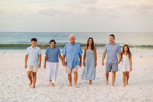 Family of six walking hand-in-hand on a sandy beach at sunset, dressed in coordinating blue and white outfits.